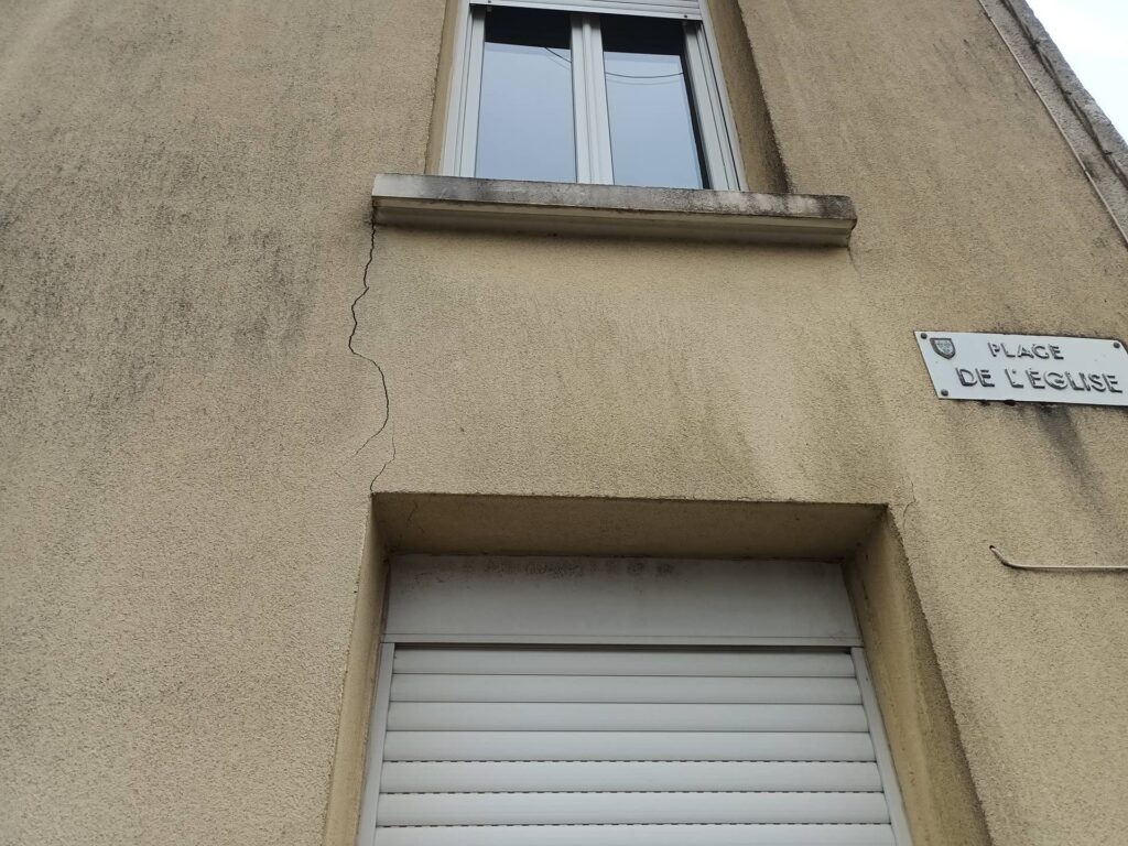 Large fissure de type lézarde sur une façade, traversant l’enduit et indiquant un mouvement structurel du bâtiment.